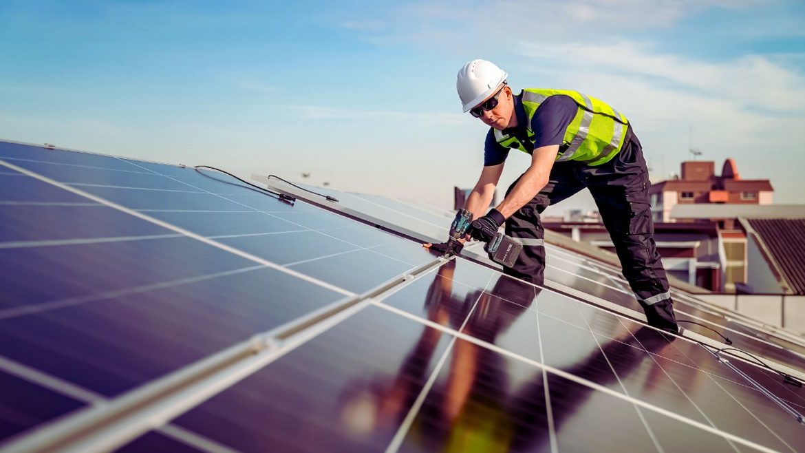 Homme installant des panneaux solaires sur un toit par beau temps
