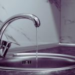 Robinet de cuisine en chrome laissant couler un filet d eau dans un evier inox