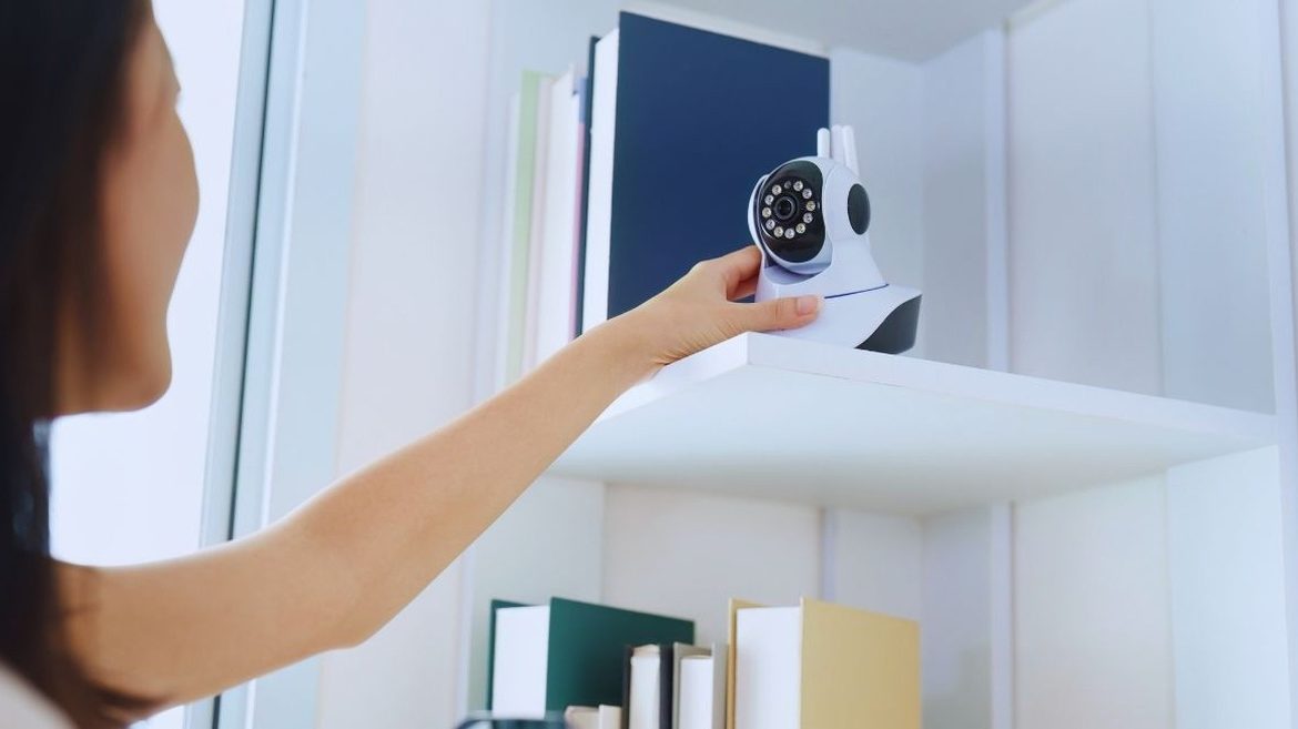 Femme qui ajuste une caméra de surveillance connectée posée sur une étagère du salon