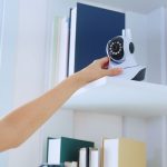 Femme qui ajuste une caméra de surveillance connectée posée sur une étagère du salon